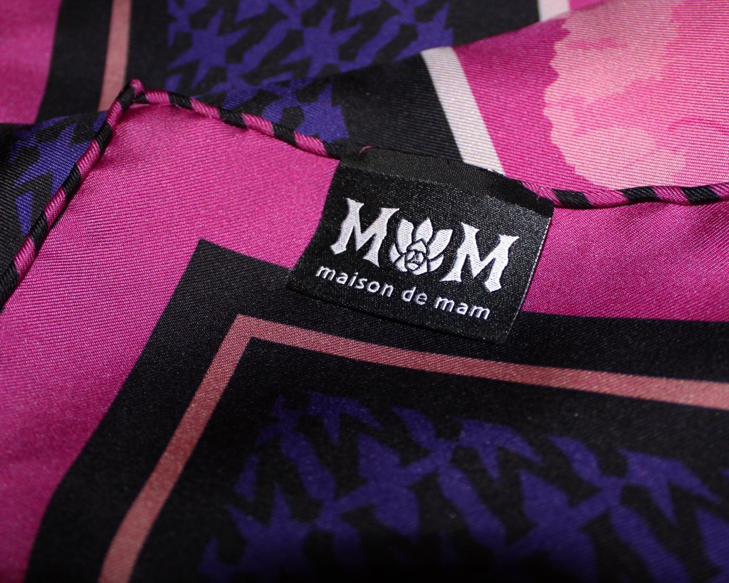 Close-up of a fabric featuring a vibrant pattern in shades of pink and purple, with a black label displaying 'M M' and 'maison de mam'.